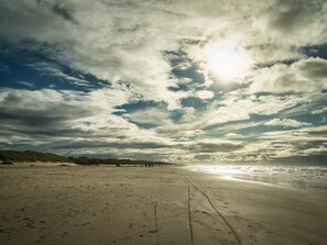 A beach with footprints leading towards the water, under a partly cloudy sky.