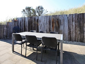 An outdoor patio with a table and chairs, a wooden fence in the background, and a clear sky. - 4 Star Holiday Home in Lokken (Lokken)
