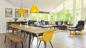 Una sala de estar moderna con comedor, que presenta un amplio sofá, sillas amarillas y una mesa de comedor de madera.