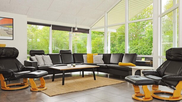 Una sala de estar moderna con un sofá modular, dos sillones, una mesita de centro y una alfombra. Amplias ventanas ofrecen vistas a zonas verdes.