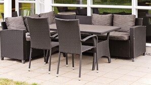 Un patio al aire libre con mobiliario de mimbre, incluyendo una mesa y sillas, y un banco incorporado.
