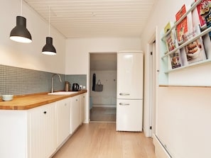 Eine Küche mit weißen Schränken, einer Holz Arbeitsplatte, einem Zwei-Türen-Kühlschrank und Pendelleuchten.