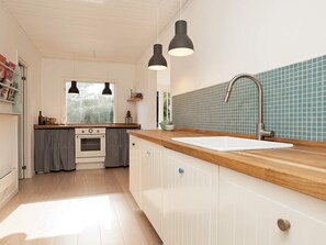 A modern kitchen with a wooden countertop, a white sink, and a stainless steel faucet. There are two pendant lights above the sink and a window with curtains.