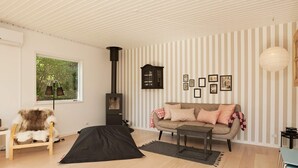 A cozy living room with a sofa, a small table, a fur chair, a fireplace, and a window with a view of greenery. - 4 Star Holiday Home in Vejby (Vejby)