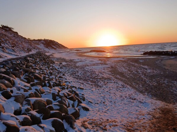 A rocky shoreline with snow-covered rocks and a sunset over the ocean.