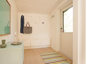 A hallway with a wooden floor, a striped rug, a door with a window, and a wall-mounted lamp.