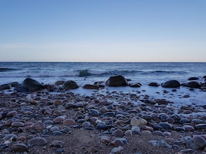 A rocky beach with waves, pebbles, and a clear sky.