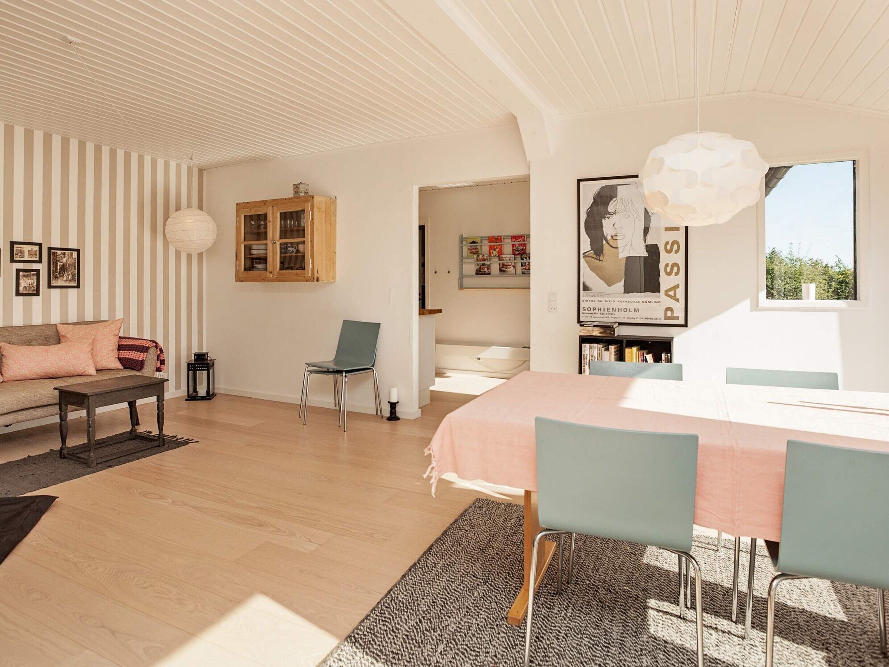 A modern living room with a sofa, a dining table with chairs, a bookshelf, and a large window.