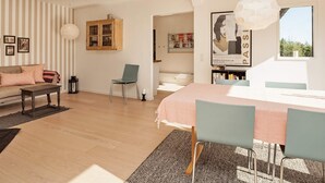 A modern living room with a sofa, a dining table with chairs, a bookshelf, and a large window. - 4 Star Holiday Home in Vejby (Vejby)