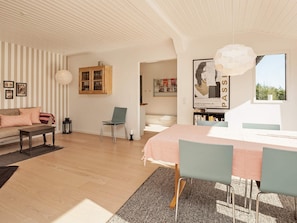 Ein modernes Wohnzimmer mit einer Couch, einem Esstisch mit Stühlen, einem Bücherregal und einem großen Fenster.