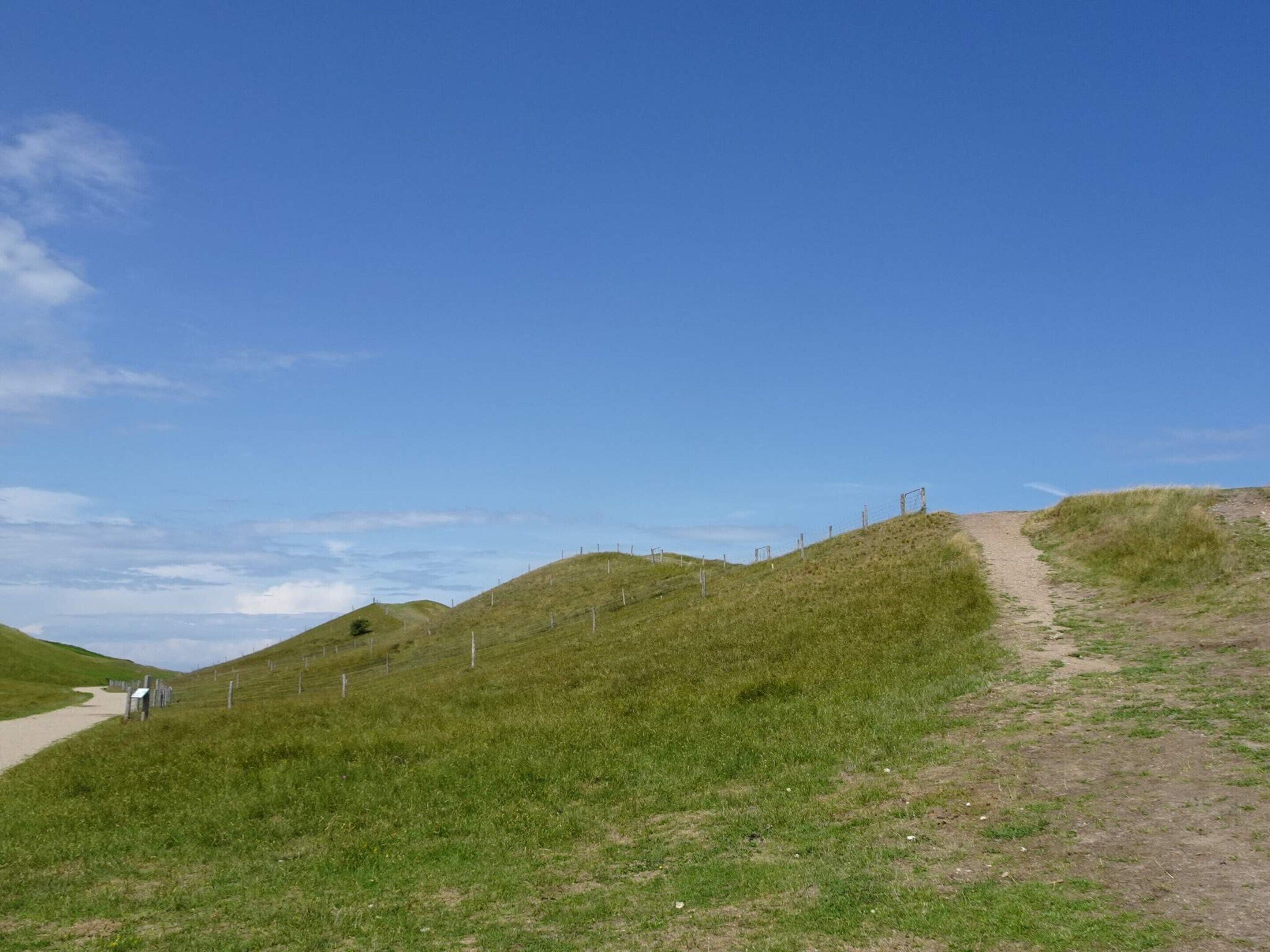 A grassy path leading up a hill with a fence and a signpost.