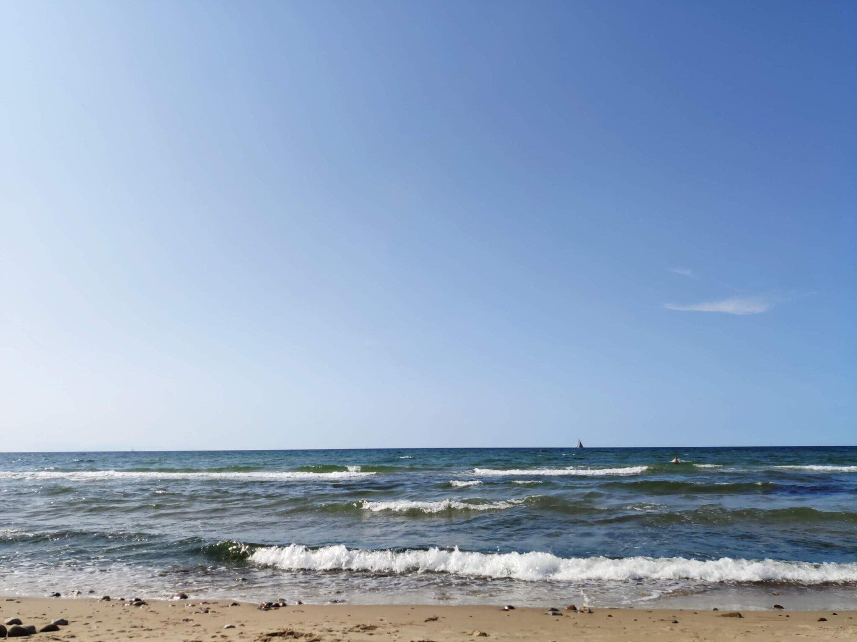 A beach with waves, a clear sky, and a distant sailboat.