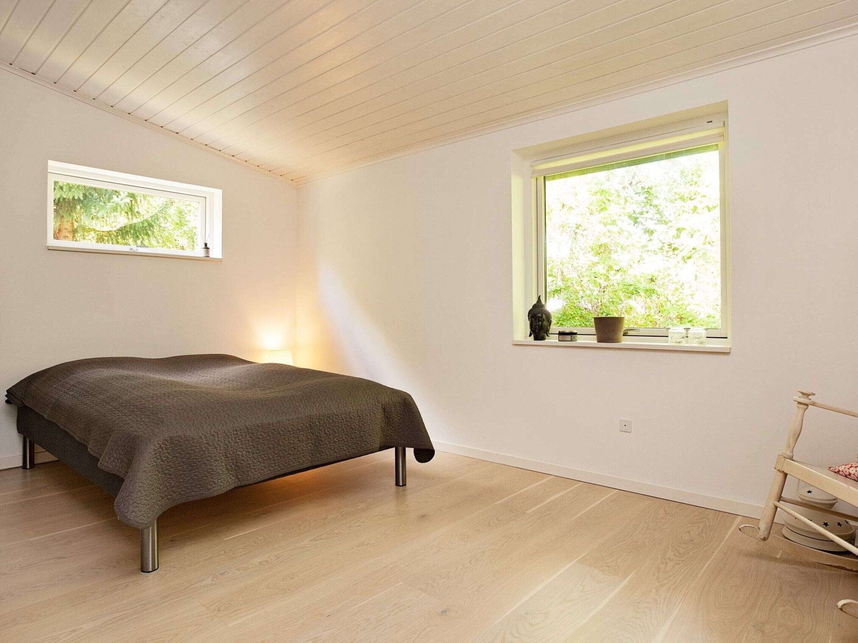 A room with a bed, a window with a view of greenery, and a shelf with items.