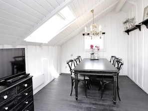 A dining area with a long table, chairs, a chandelier, and a television on a dresser.