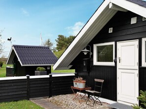 A black wooden building with a sloped roof, a white door, and a small outdoor seating area with a table and chairs.
