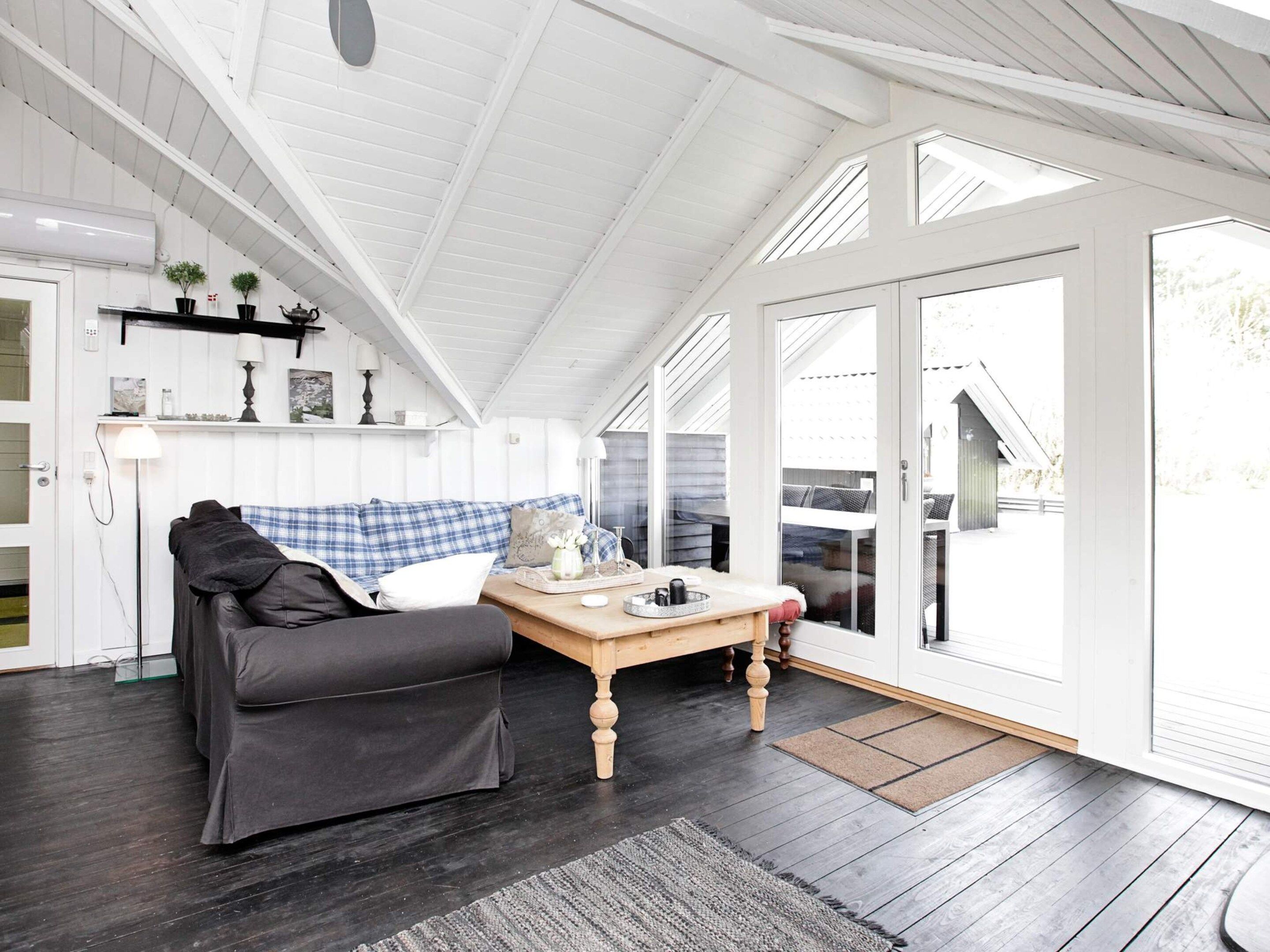 A cozy room with a dark wooden floor, a blue plaid sofa, a wooden coffee table, and a large window with a view of the outdoors.