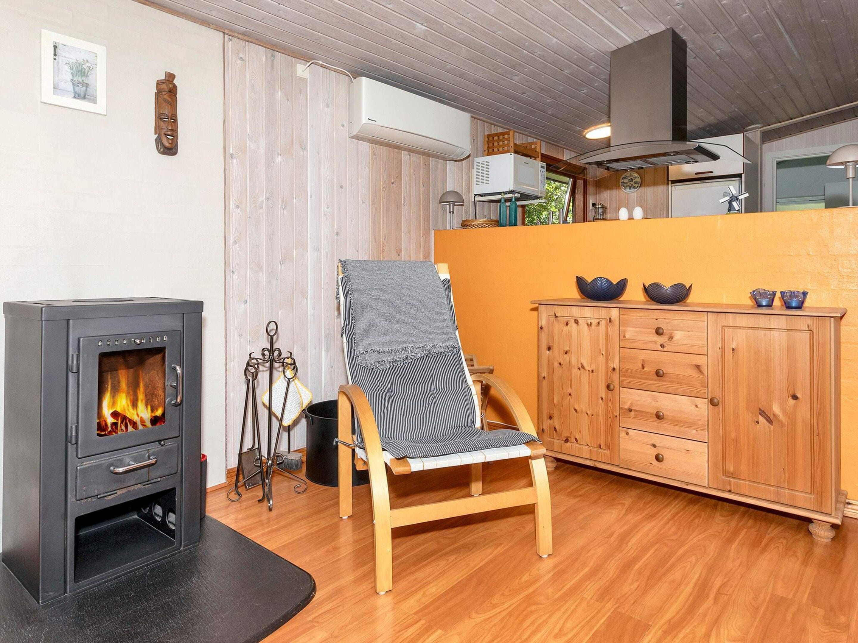 A cozy room with a wood-burning stove, a wooden chair, a cabinet, and a window.