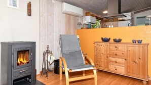 A cozy room with a wood-burning stove, a wooden chair, a cabinet, and a window. - 4 Star Holiday Home in Lokken (Lokken)