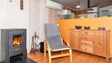 A cozy room with a wood-burning stove, a wooden chair, a cabinet, and a window.