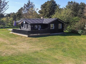 A single-story building with a dark exterior, a covered porch, and a fenced yard. - 4 Star Holiday Home in Lokken (Lokken)