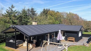 A cabin with a covered deck, outdoor seating, and a swing set. - 4 Star Holiday Home in Lokken (Lokken)