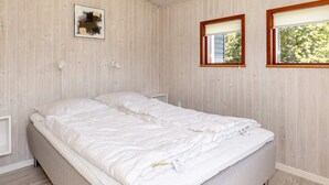 A bedroom with a double bed, wooden walls, a window with blinds, and a wall-mounted light fixture. - 4 Star Holiday Home in Lokken (Lokken)
