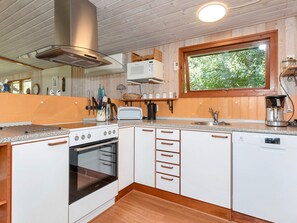 A modern kitchen with a built-in oven, a coffee maker, and a window providing a view of greenery.