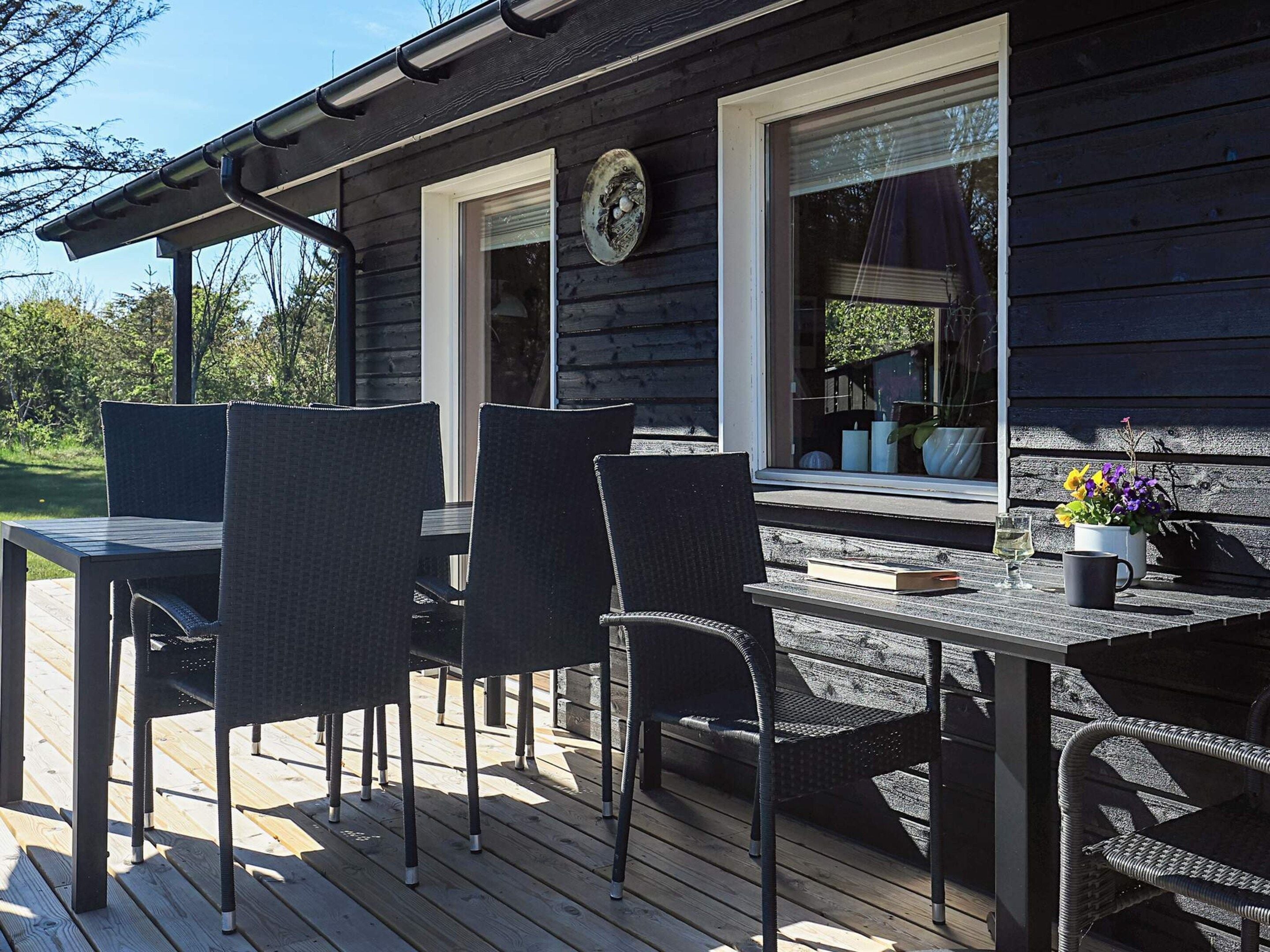 A wooden deck with a table and chairs, a window with a clock, and a potted plant.