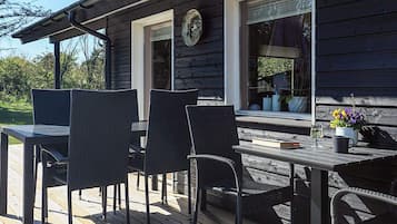 A wooden deck with a table and chairs, a window with a clock, and a potted plant.