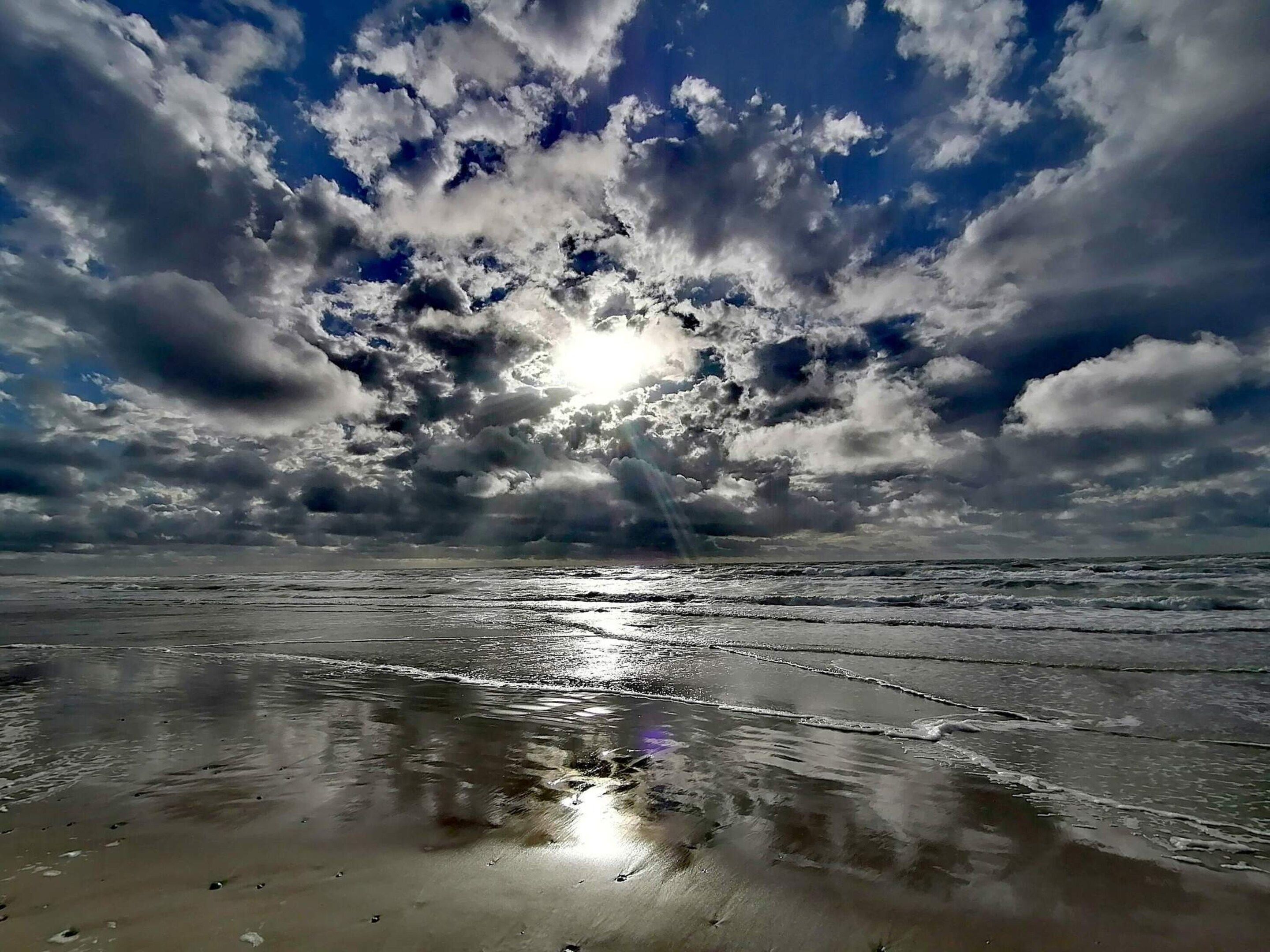 A beach with waves, a cloudy sky, and sunlight.