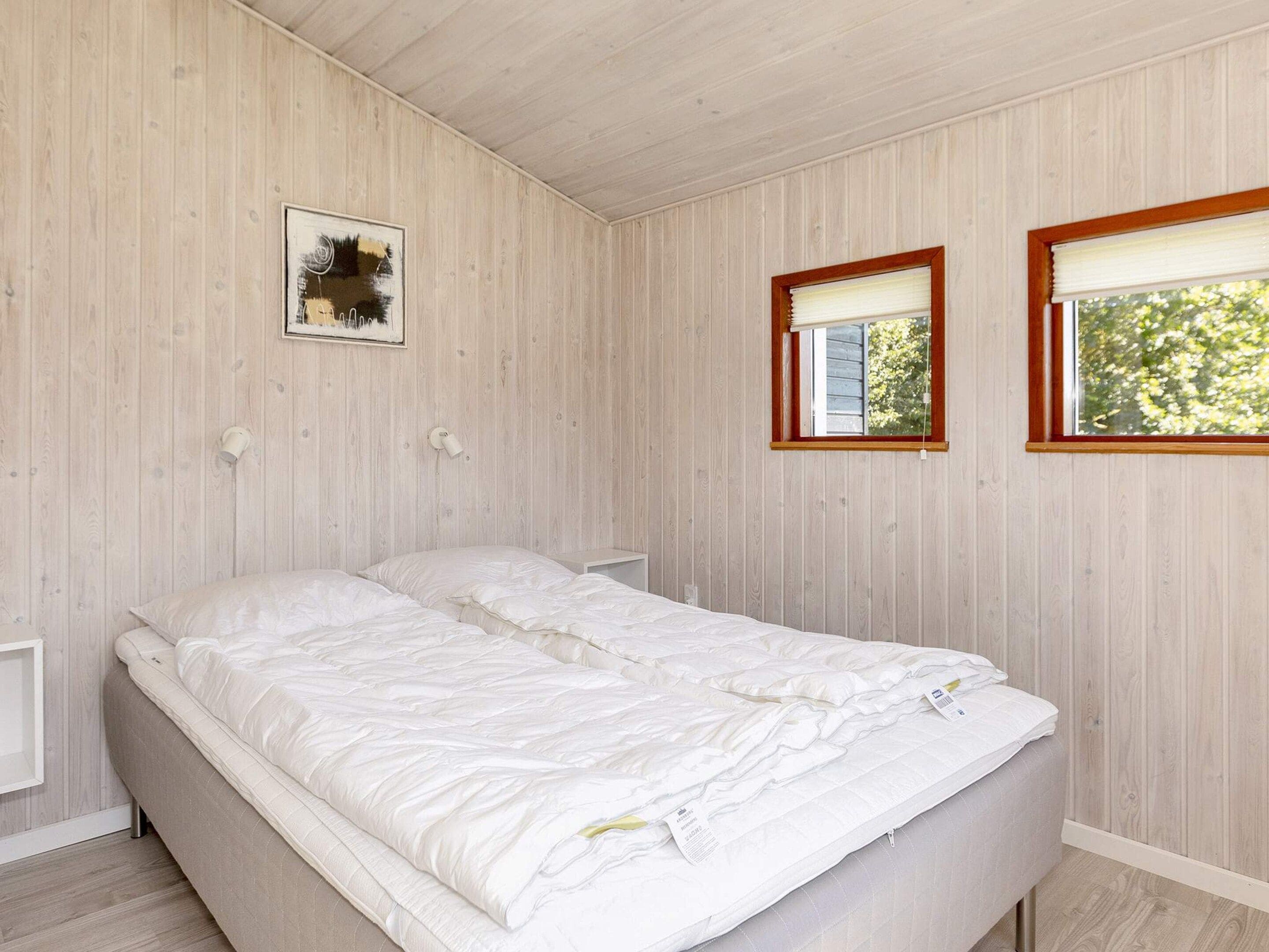 Un dormitorio con cama doble, paredes de madera, un ventanal con persianas y una lámpara fijada a la pared.