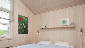 A bedroom with a wooden ceiling, a bed with white bedding, a poster of Van Gogh Museum, and a shelf with books and a bird figurine. - Winsome Holiday Home in Blokhus near Sea (Blokhus)
