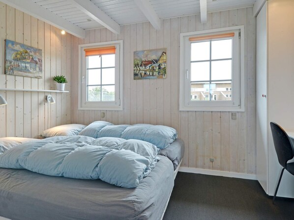 Une chambre à coucher avec un lit, deux fenêtres et des œuvres d’art accrochées aux murs.