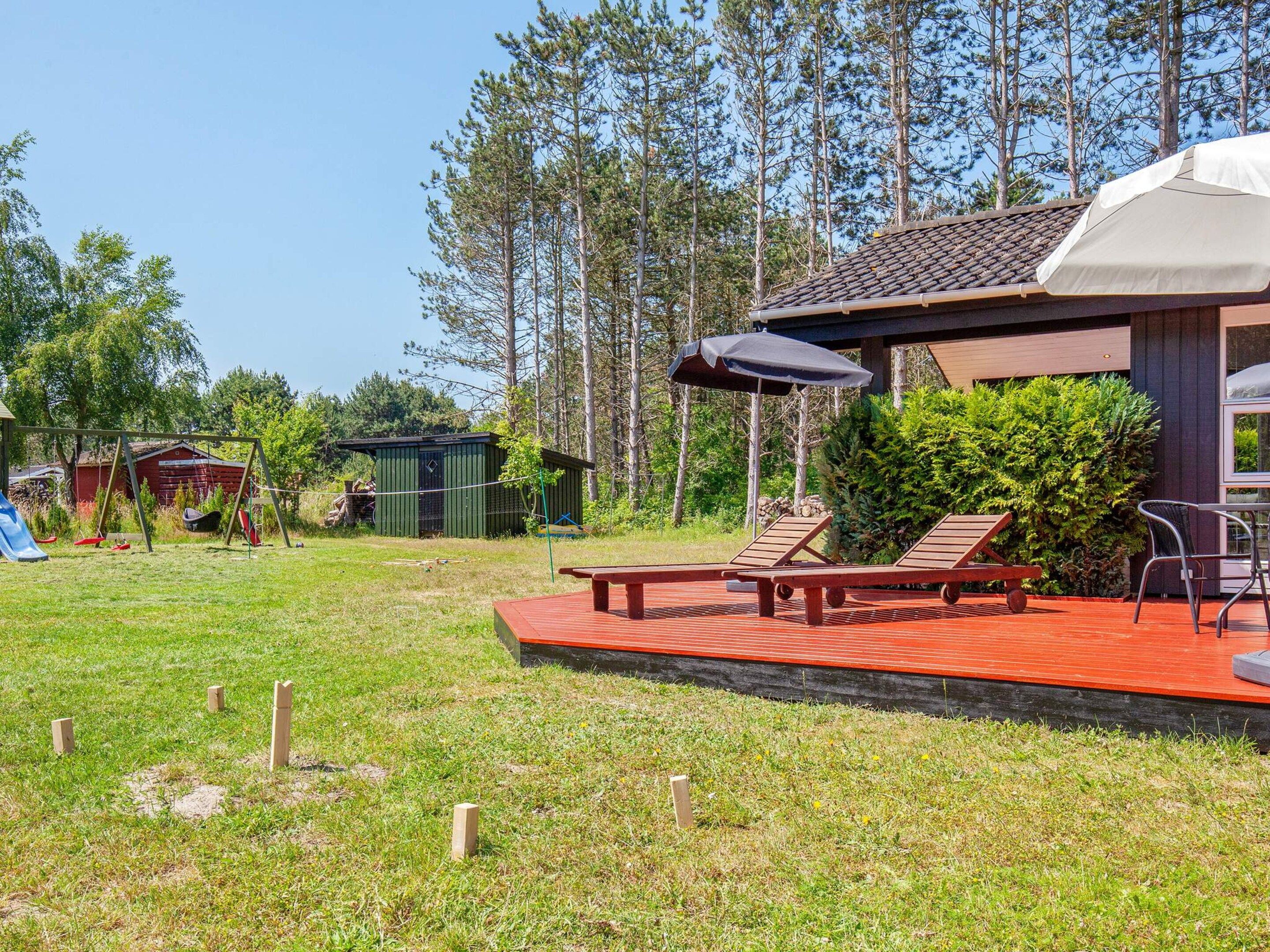 A deck with lounge chairs and a picnic table, surrounded by a grassy yard and trees.