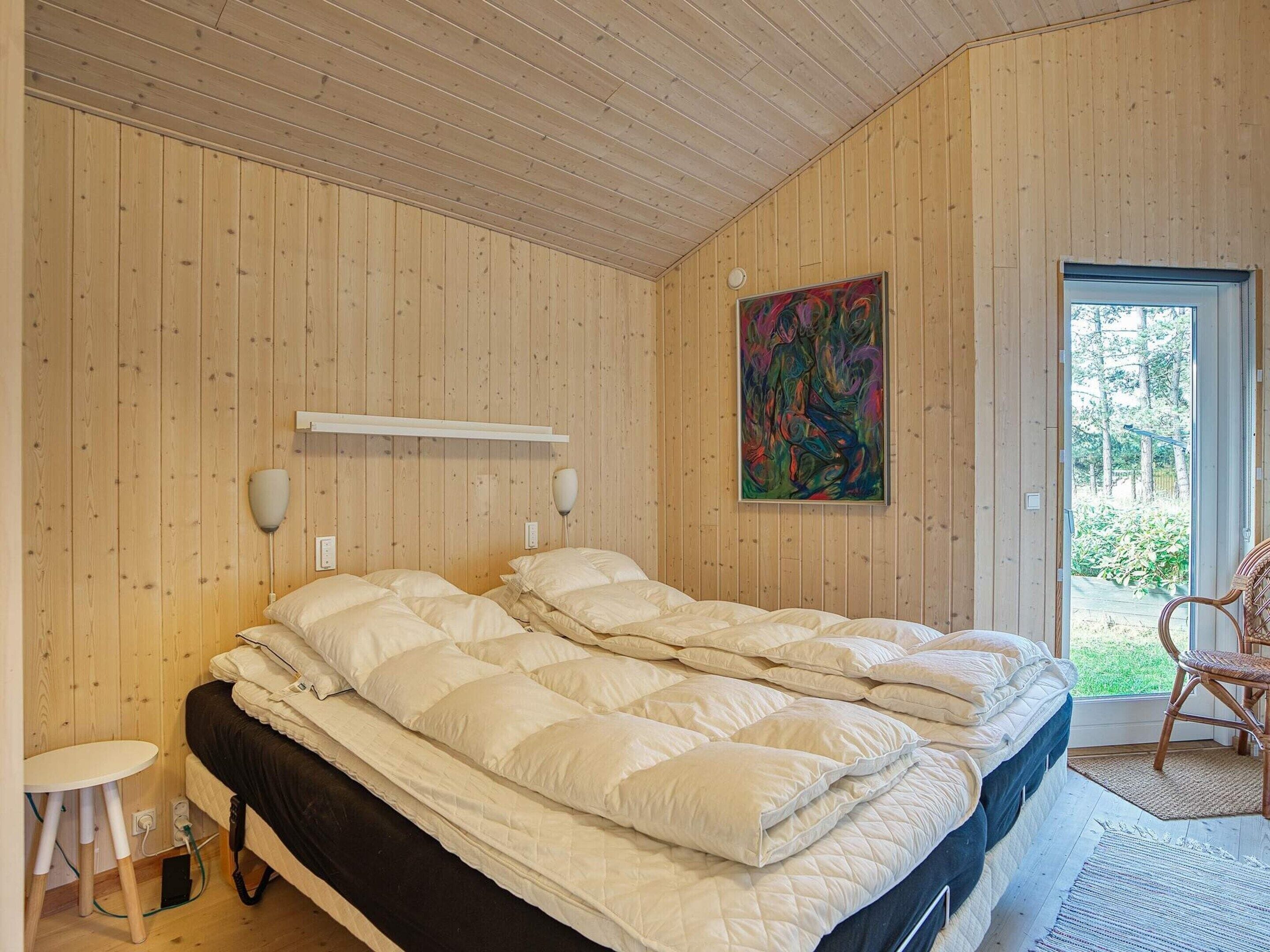 Ein Zimmer mit einem Bett, einem Sessel, einem Gemälde und einer Tür, die nach draußen führt.