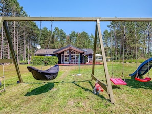 Ein Spielplatz mit einer Holzschaukel, einem hängenden Sitz und zwei Schaukeln mit roten Sitzen.