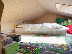 A small, wooden-paneled room with a single bed, a desk with a computer, and a window.