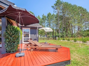 A wooden deck with a red floor, two lounge chairs, a small table, and a large umbrella providing shade.