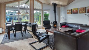 A spacious living area with a fireplace, leather furniture, and large windows offering a view of the outdoors. - 5 Star Holiday Home in Rodby (Rodby)