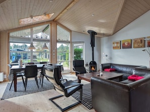 A spacious living area with a fireplace, leather furniture, and large windows offering a view of the outdoors. - 5 Star Holiday Home in Rodby (Rodby)