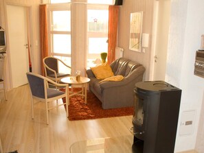 A living room with a sofa, chairs, a small table, a fireplace, and a window with curtains. - Holiday Home in Otterndorf (Otterndorf)
