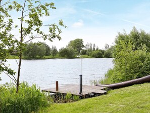 A wooden dock extending into a calm lake, surrounded by lush greenery and trees. - Holiday Home in Otterndorf (Otterndorf)
