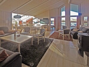 A spacious living area with a fireplace, multiple seating arrangements, and large windows offering views. - Holiday Home in Otterndorf (Otterndorf)