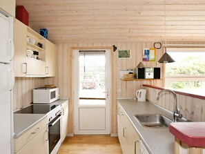 A compact kitchen with wooden walls, a microwave, a stove, a sink, and a window with a view of the outside.