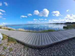 A wooden boardwalk leading to a calm body of water with a clear sky.