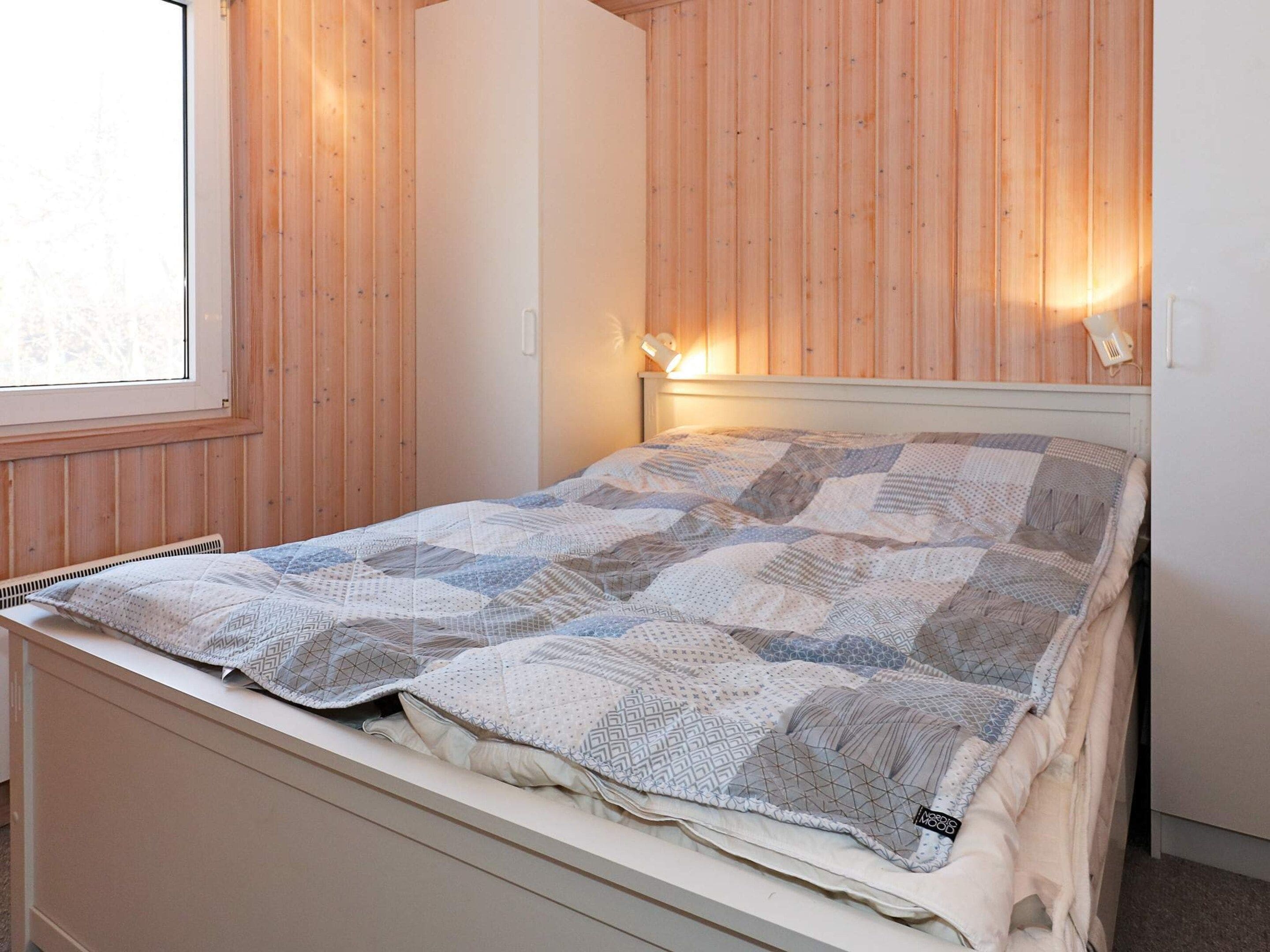A bed with a quilt in a room with wooden walls and a window.