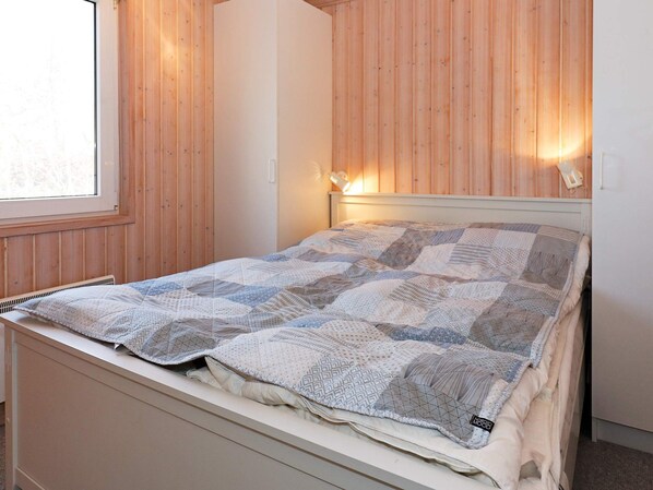 A bed with a quilt in a room with wooden walls and a window.