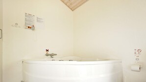 A bathroom with a large bathtub, a toilet, and a trash can. - 5 Star Holiday Home in Hadsund (Hadsund)