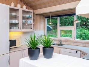 A kitchen with wooden cabinets, a microwave, a sink, and two potted plants on the counter. - Secluded Holiday Home in Henne near Beach (Henne)