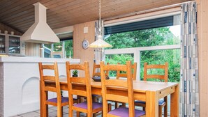 A dining area with a wooden table and chairs, a hanging light fixture, a clock on the wall, and a window with a view of greenery. - Secluded Holiday Home in Henne near Beach (Henne)